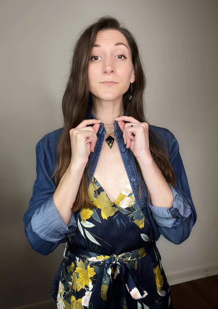 Bri shows off her necklace styled under the collar of a chambray blouse layered over a satin floral jumpsuit for a casual outfit made more formal