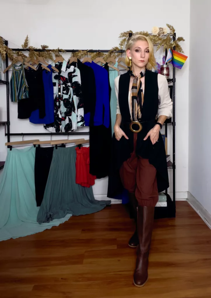 Bri showcases a causal pirate inspired outfit with a long assymetical vest, brown boots, and large buckled belt, and a printed brown, black, and cream silk scarf