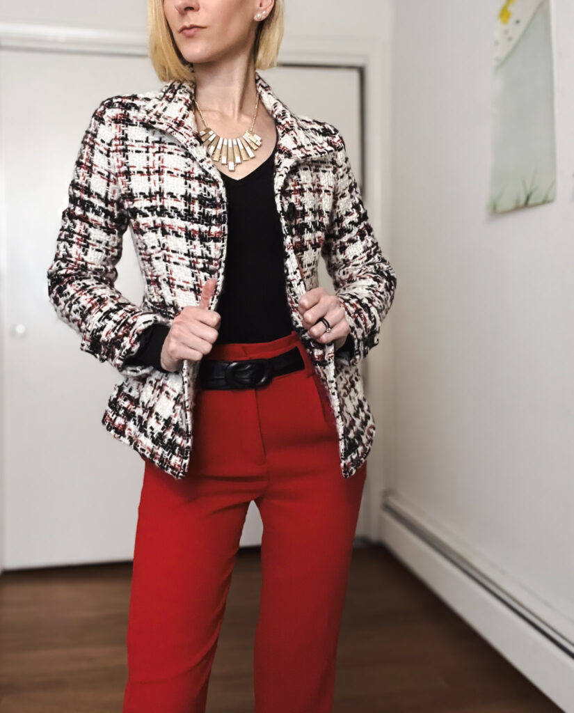 Bri shows off her winter layers and newly thrifted outfit with red high waisted trousers, a black knit sweater, and a black and red printed coat paired with a gold and silver necklace